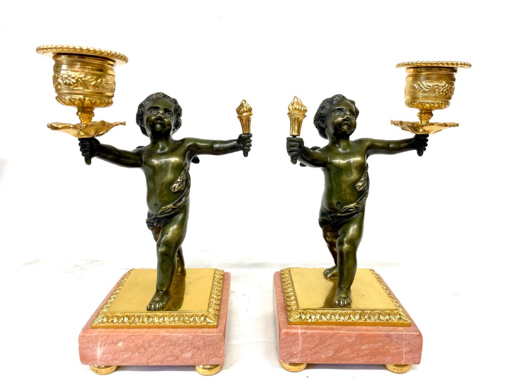 A three-piece antique French garniture set featuring a pink marble and gilt bronze mantel clock flanked by two bronze cherub candelabra. View XVII