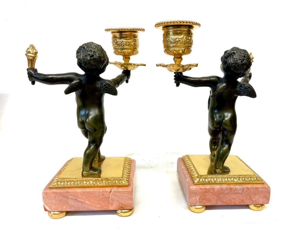 A three-piece antique French garniture set featuring a pink marble and gilt bronze mantel clock flanked by two bronze cherub candelabra. View XVIII