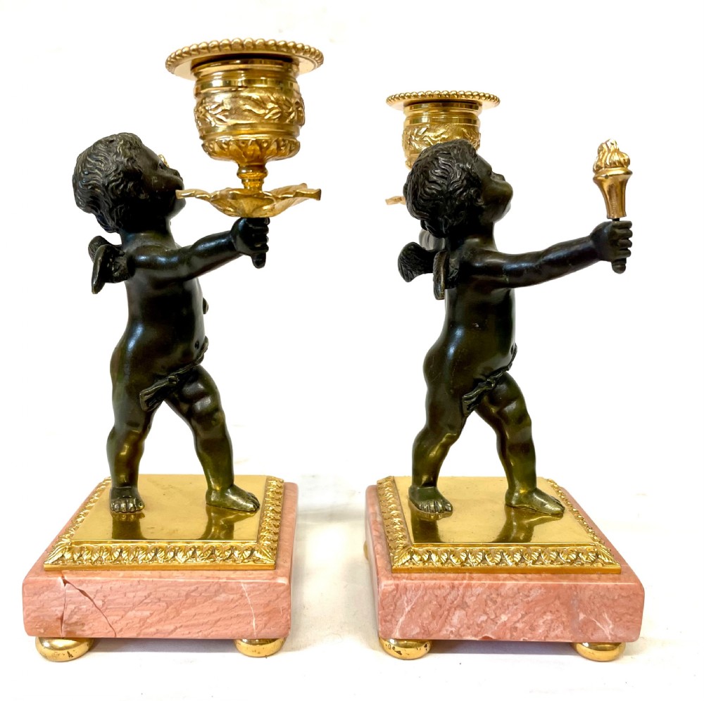 A three-piece antique French garniture set featuring a pink marble and gilt bronze mantel clock flanked by two bronze cherub candelabra. View XIX