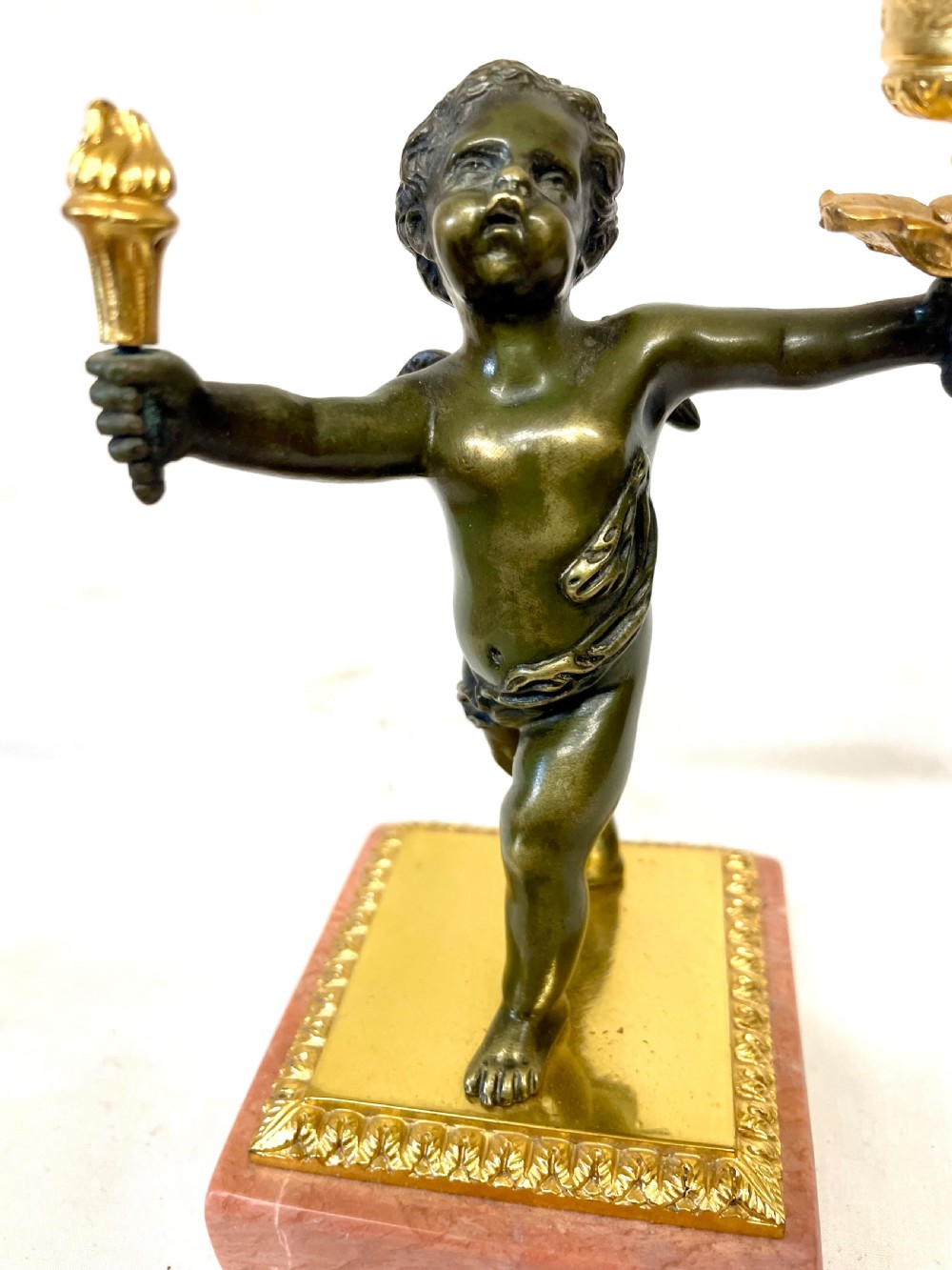 A three-piece antique French garniture set featuring a pink marble and gilt bronze mantel clock flanked by two bronze cherub candelabra. View XXI