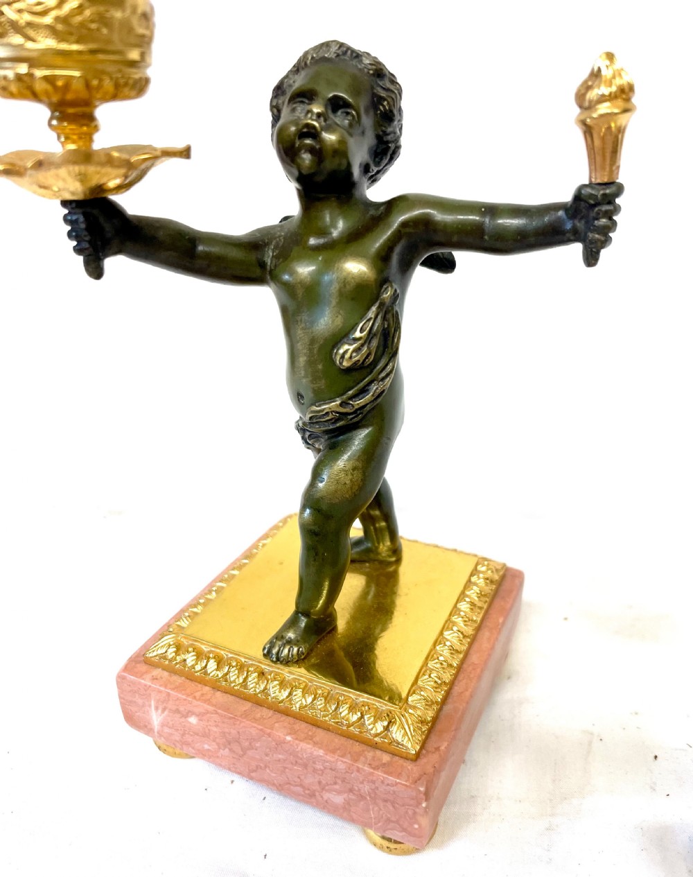 A three-piece antique French garniture set featuring a pink marble and gilt bronze mantel clock flanked by two bronze cherub candelabra. View XXII