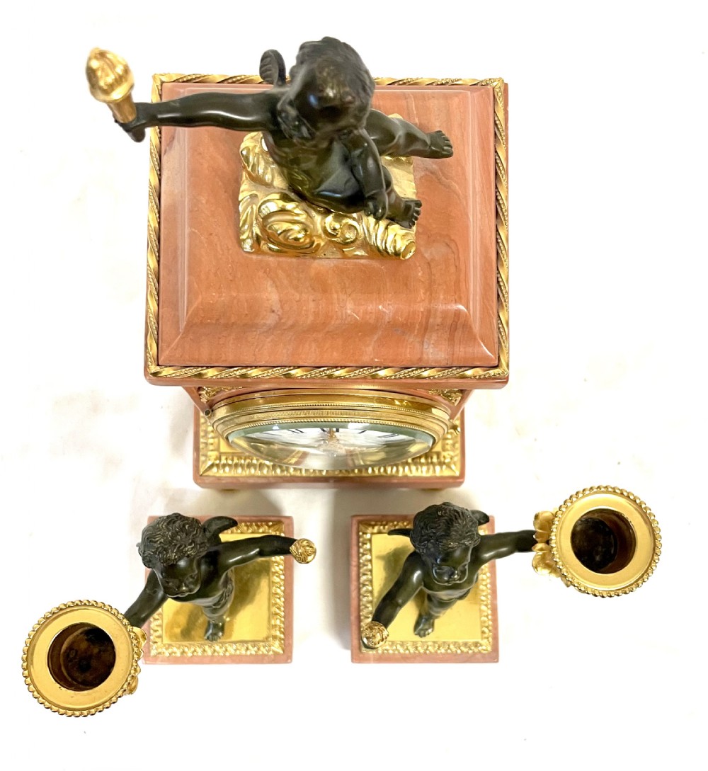 A three-piece antique French garniture set featuring a pink marble and gilt bronze mantel clock flanked by two bronze cherub candelabra. View XXIII