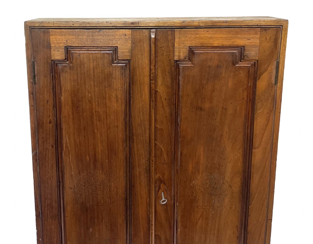 An antique cedar wood wall cabinet featuring two panelled doors with faint engraved H. Upmann Habana cigar branding and a central keyhole. View II