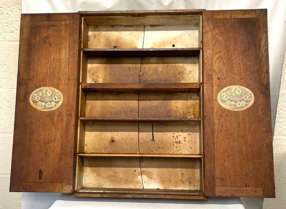 An antique cedar wood wall cabinet featuring two panelled doors with faint engraved H. Upmann Habana cigar branding and a central keyhole. View VIII