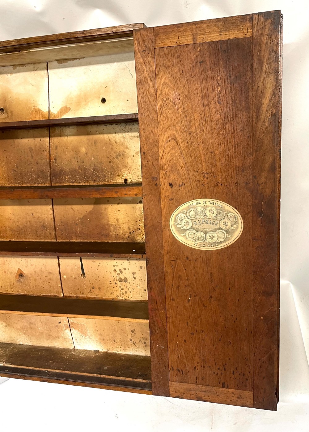 An antique cedar wood wall cabinet featuring two panelled doors with faint engraved H. Upmann Habana cigar branding and a central keyhole. View IX
