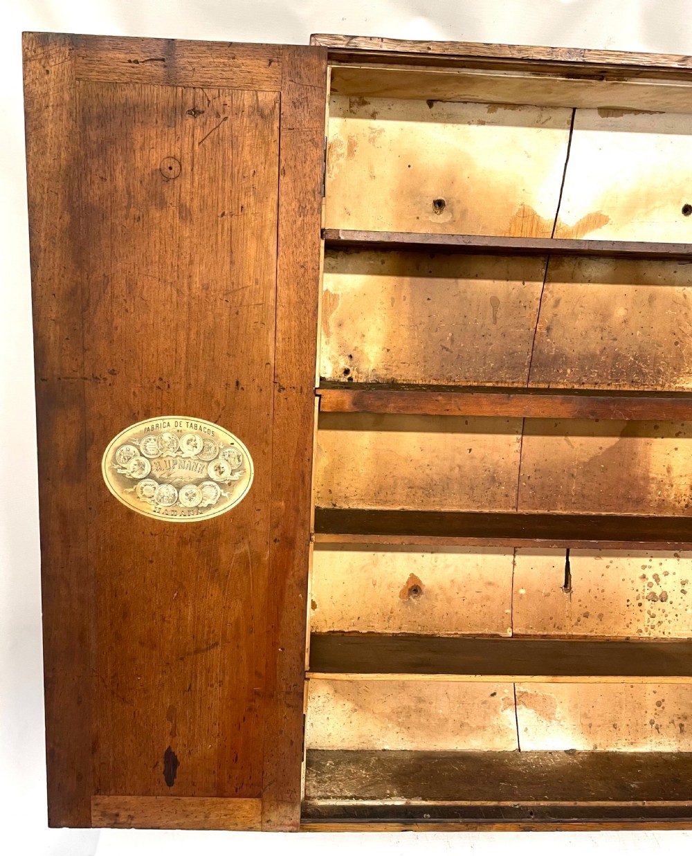 An antique cedar wood wall cabinet featuring two panelled doors with faint engraved H. Upmann Habana cigar branding and a central keyhole. View X