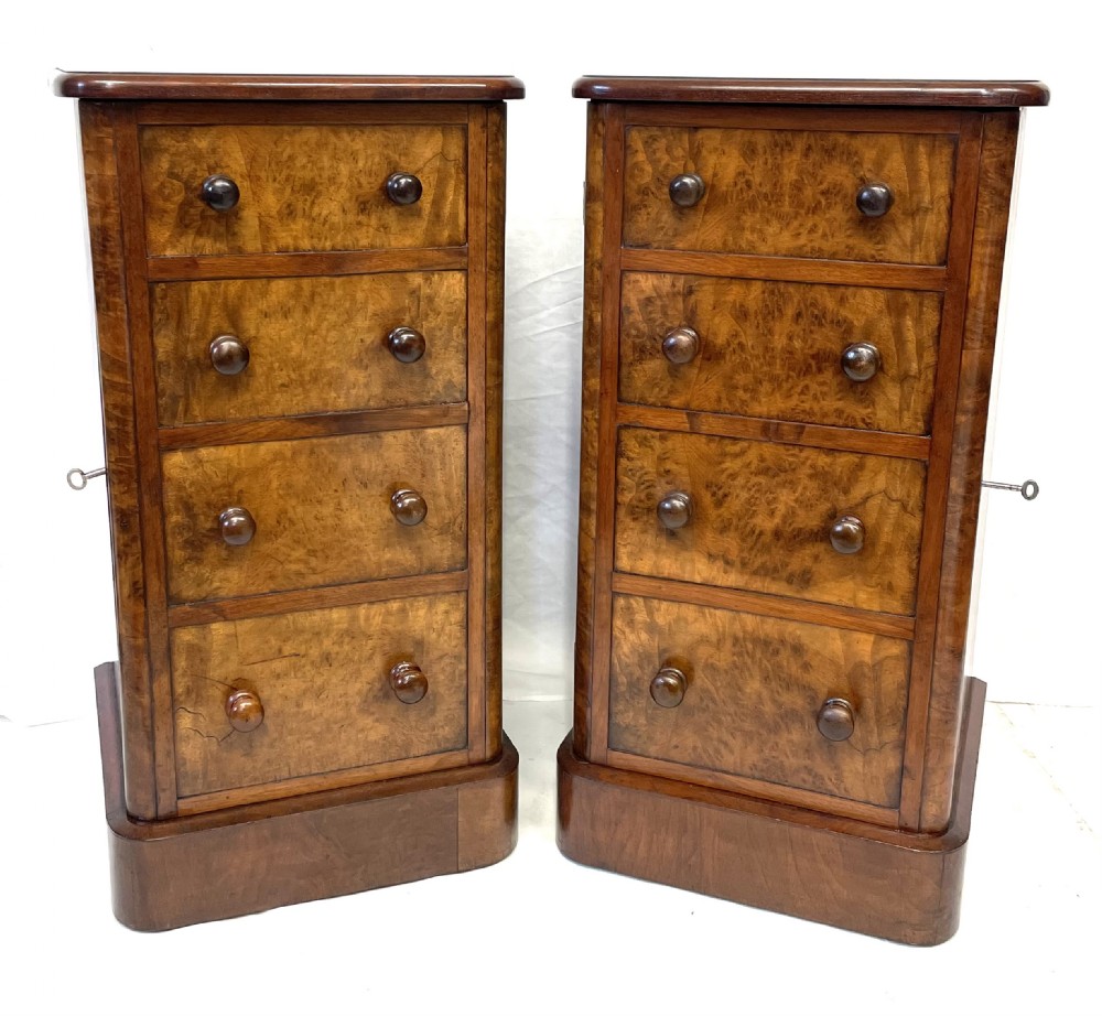 A pair of narrow Victorian burr walnut bedside cabinets featuring four drawers each, turned wooden handles, side locking mechanisms, and plinth bases.