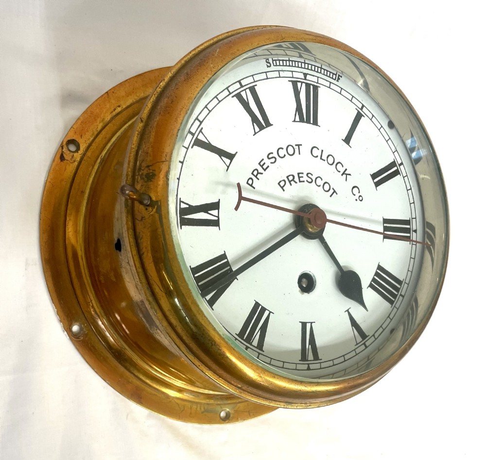 A circular brass-cased ship clock with a white dial displaying black Roman numerals, spade hands, and the maker name Prescot Clock Co. View II
