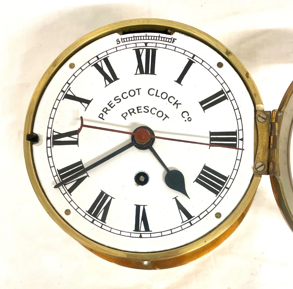 A circular brass-cased ship clock with a white dial displaying black Roman numerals, spade hands, and the maker name Prescot Clock Co. View VII