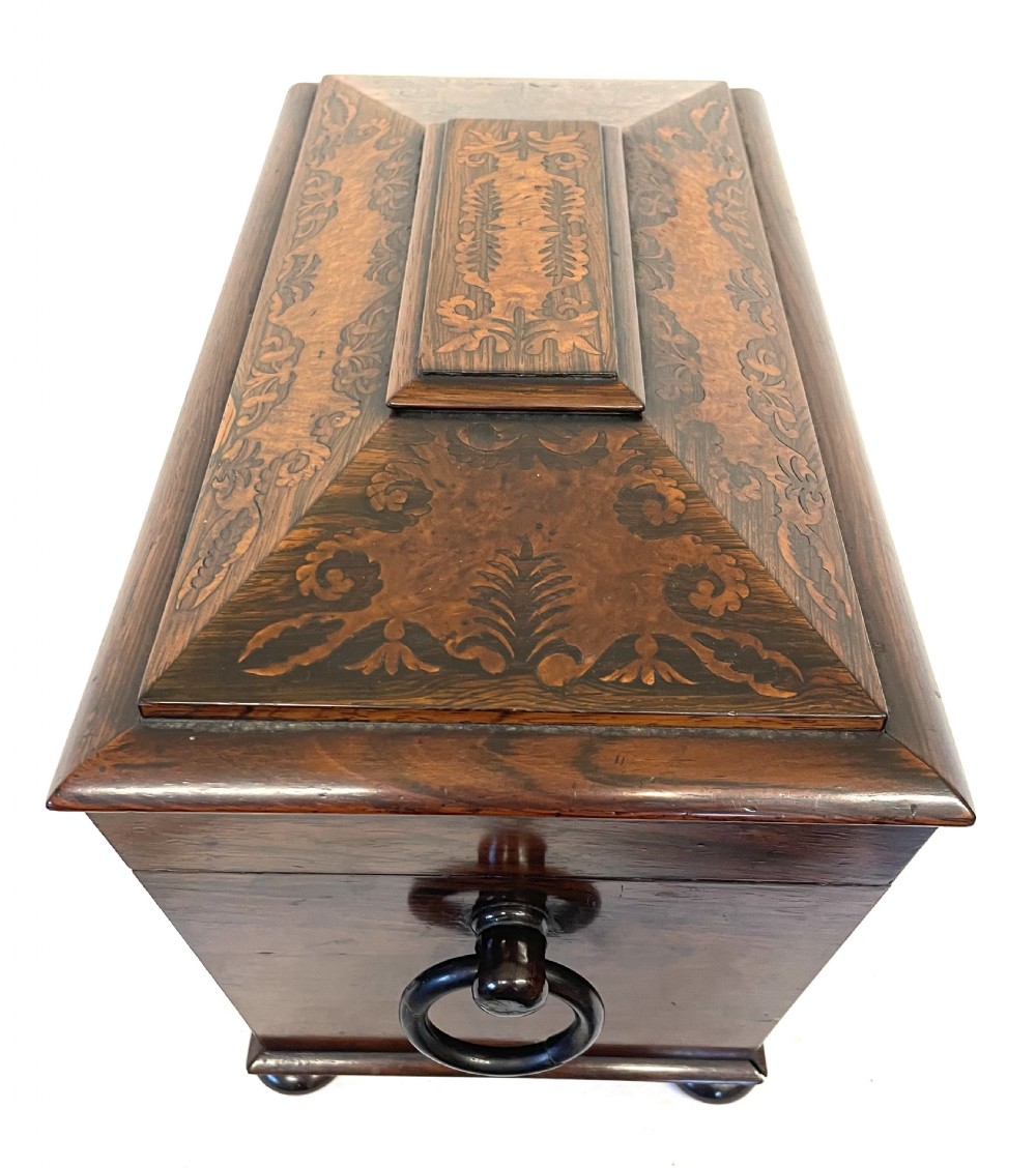 A George IV sarcophagus-shaped wooden tea caddy featuring amboyna veneers, intricate marquetry foliate inlay, a central escutcheon with key, and stepped lid construction. View XI