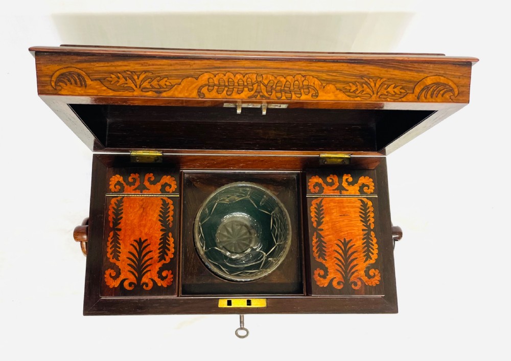 A George IV sarcophagus-shaped wooden tea caddy featuring amboyna veneers, intricate marquetry foliate inlay, a central escutcheon with key, and stepped lid construction. View XIII
