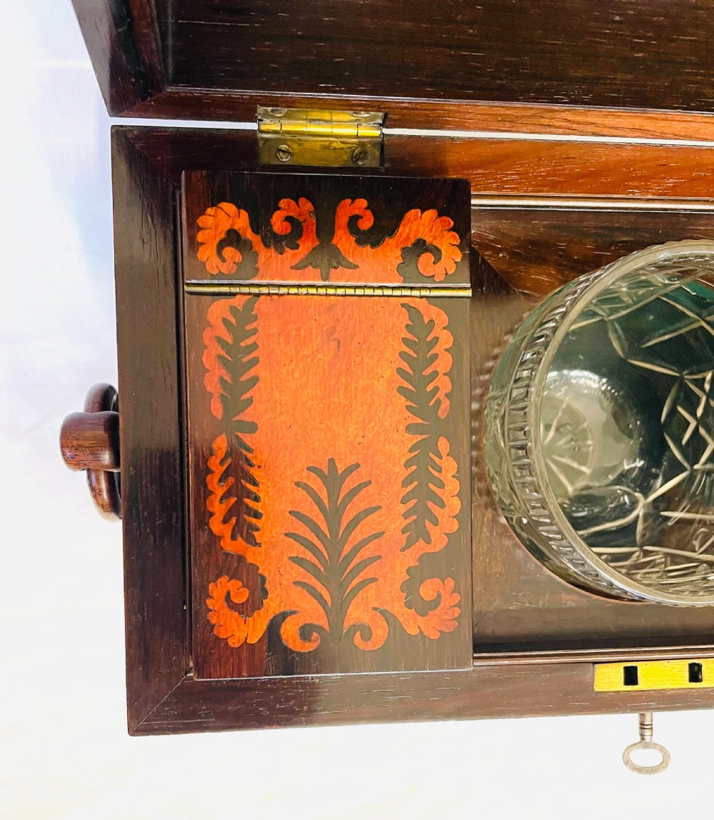 A George IV sarcophagus-shaped wooden tea caddy featuring amboyna veneers, intricate marquetry foliate inlay, a central escutcheon with key, and stepped lid construction. View XIV