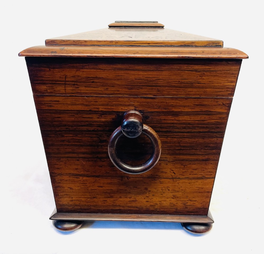 A George IV sarcophagus-shaped wooden tea caddy featuring amboyna veneers, intricate marquetry foliate inlay, a central escutcheon with key, and stepped lid construction. View XIX