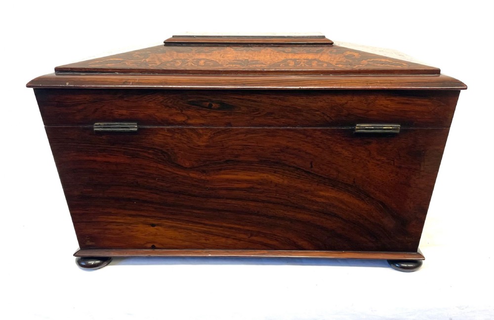A George IV sarcophagus-shaped wooden tea caddy featuring amboyna veneers, intricate marquetry foliate inlay, a central escutcheon with key, and stepped lid construction. View XXI
