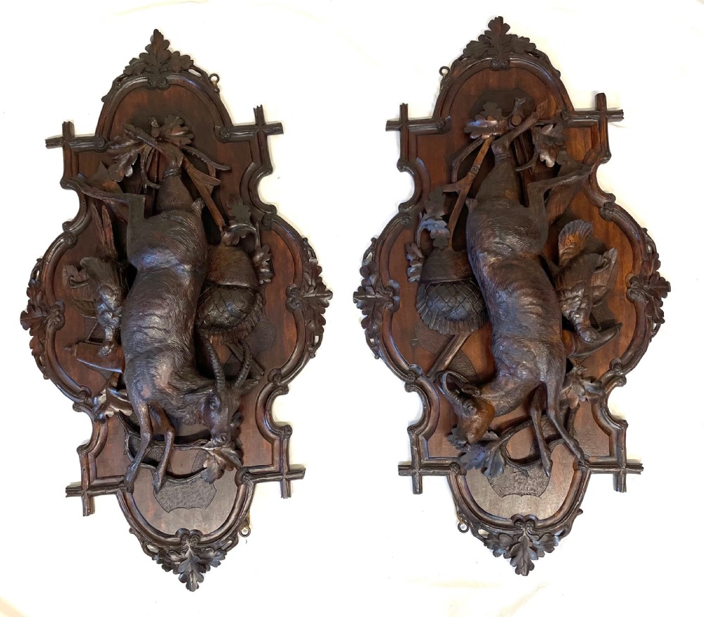 A pair of 19th-century carved dark wood wall plaques depicting hunted game, including a chamois and birds framed by oak foliage and hunting gear.