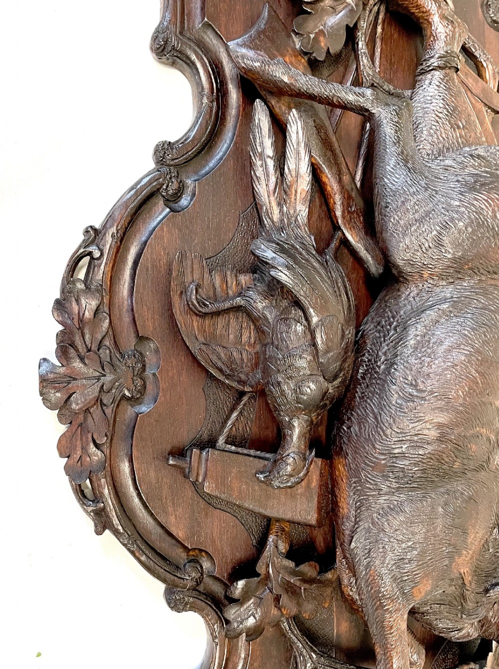 A pair of 19th-century carved dark wood wall plaques depicting hunted game, including a chamois and birds framed by oak foliage and hunting gear. View X