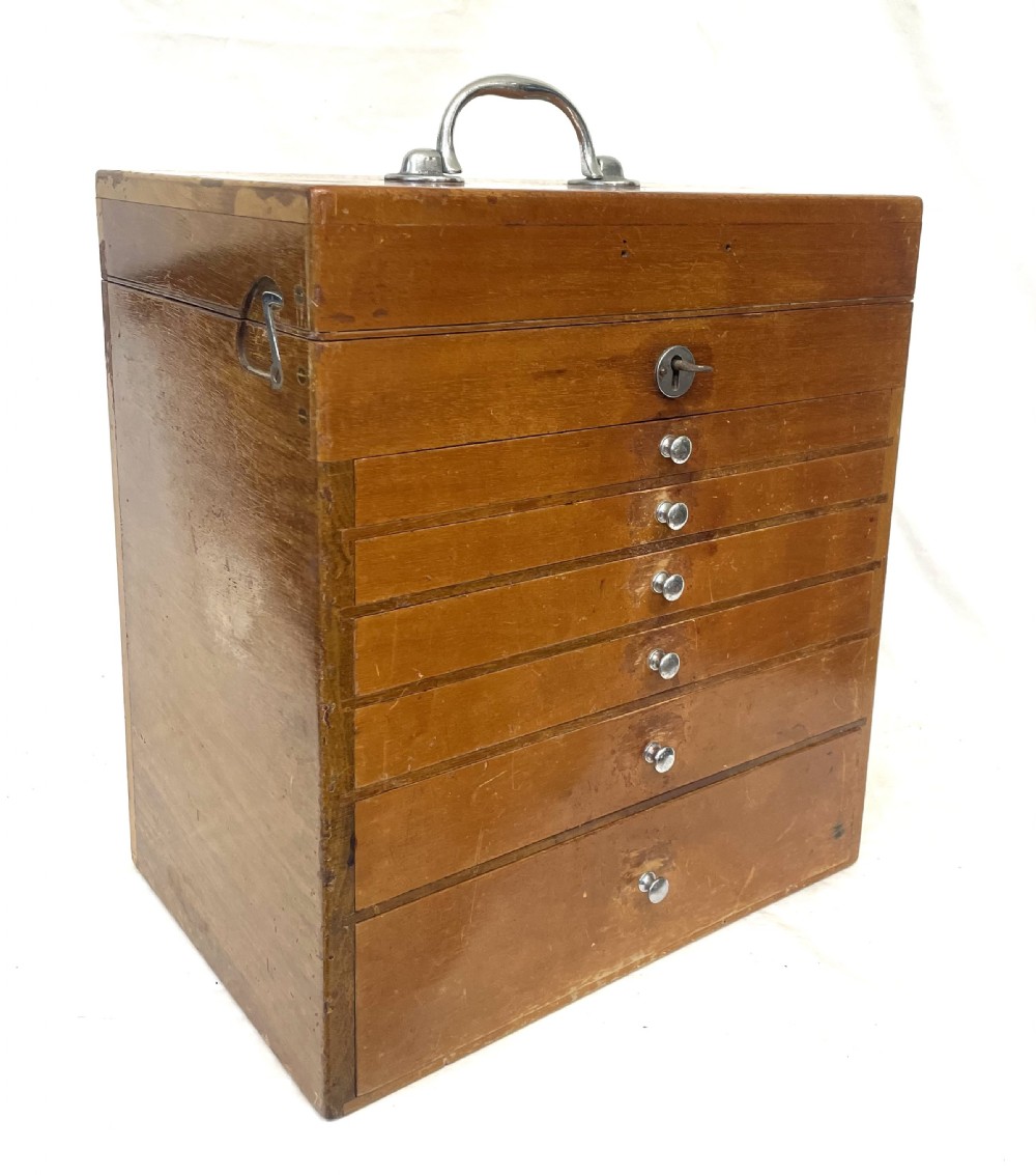 A rectangular wooden portable dental cabinet with six graduated drawers, silver-coloured metal pull knobs, a metal keyhole escutcheon, and a top carrying handle. View III