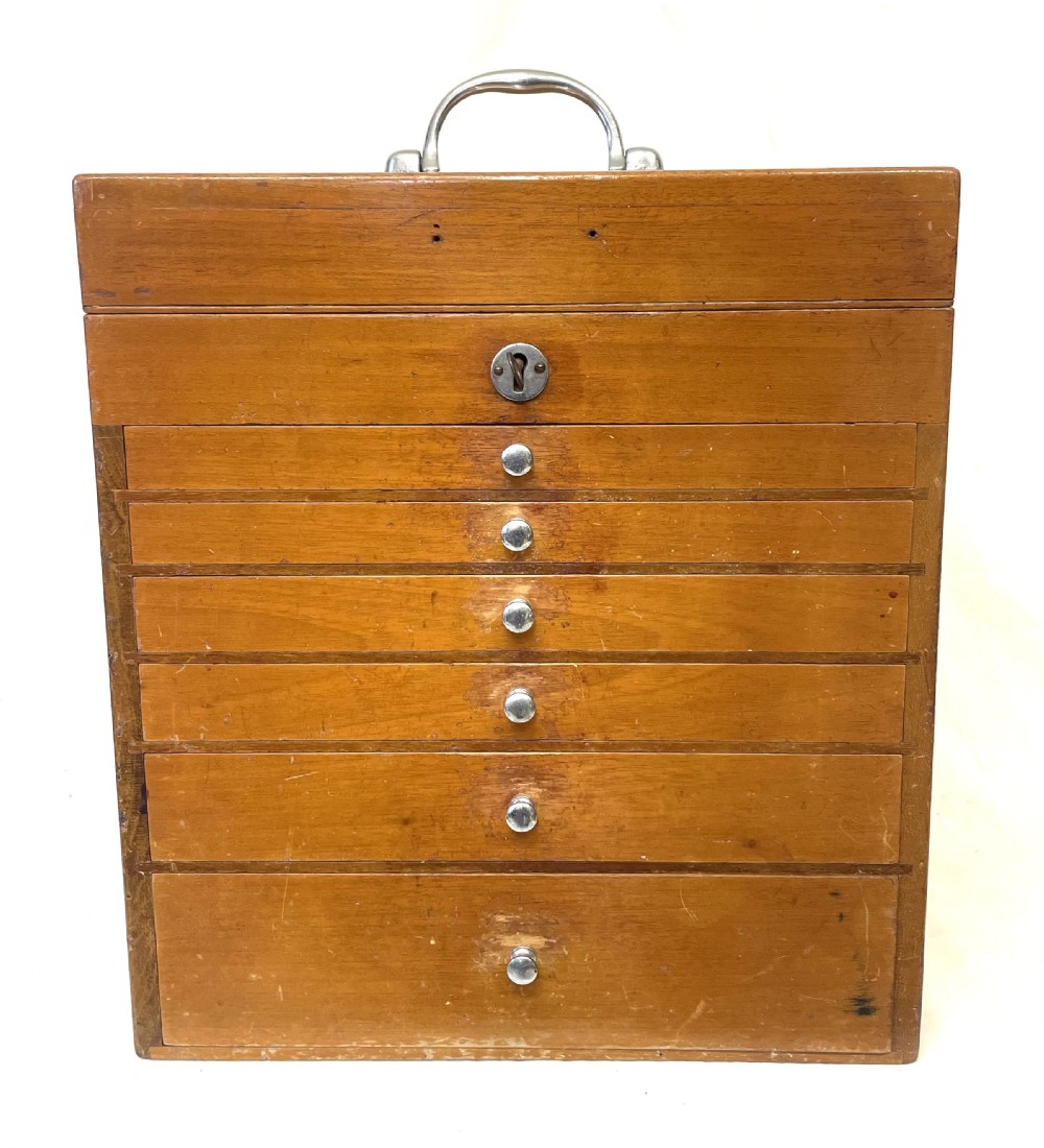 A rectangular wooden portable dental cabinet with six graduated drawers, silver-coloured metal pull knobs, a metal keyhole escutcheon, and a top carrying handle. View V