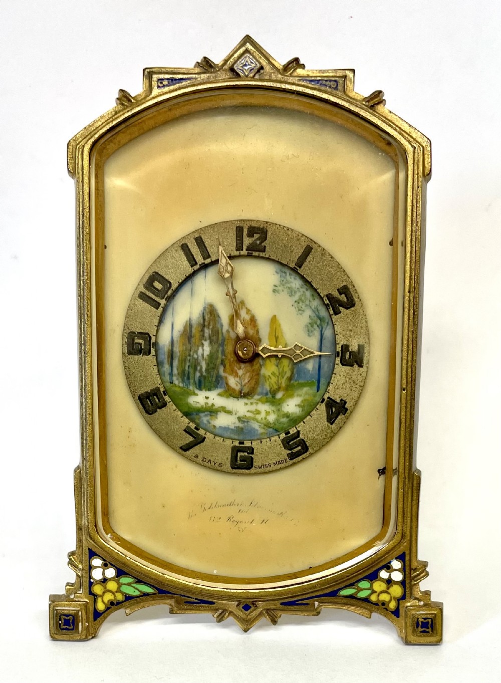 An antique miniature gilt metal easel clock featuring a painted landscape dial surrounded by champleve enamel floral decoration at the base.