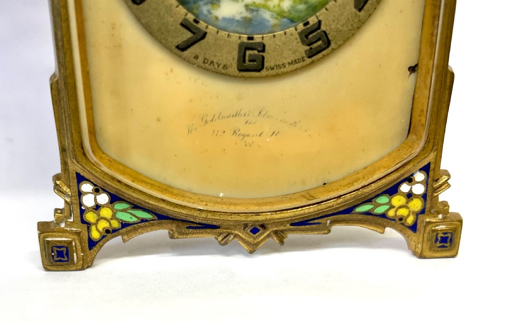 An antique miniature gilt metal easel clock featuring a painted landscape dial surrounded by champleve enamel floral decoration at the base. View X
