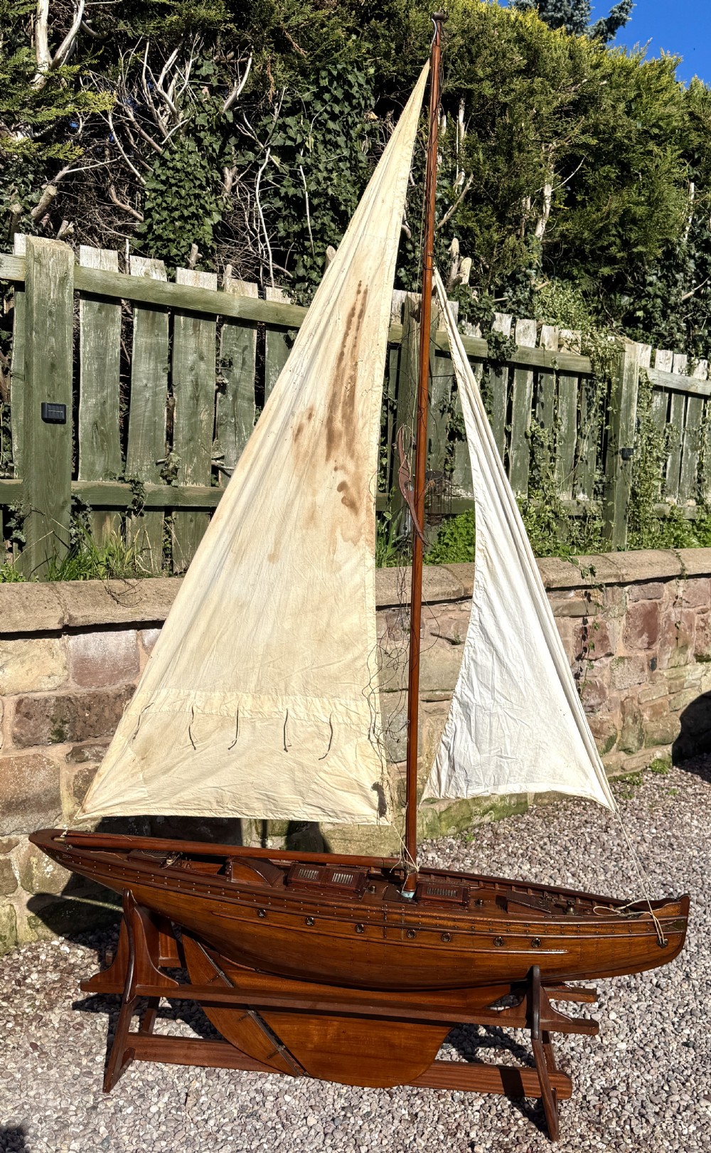 A large Victorian wooden pond yacht with stitched fabric sails, brass deck fittings, and a carved wooden keel, displayed on a wooden stand. View II