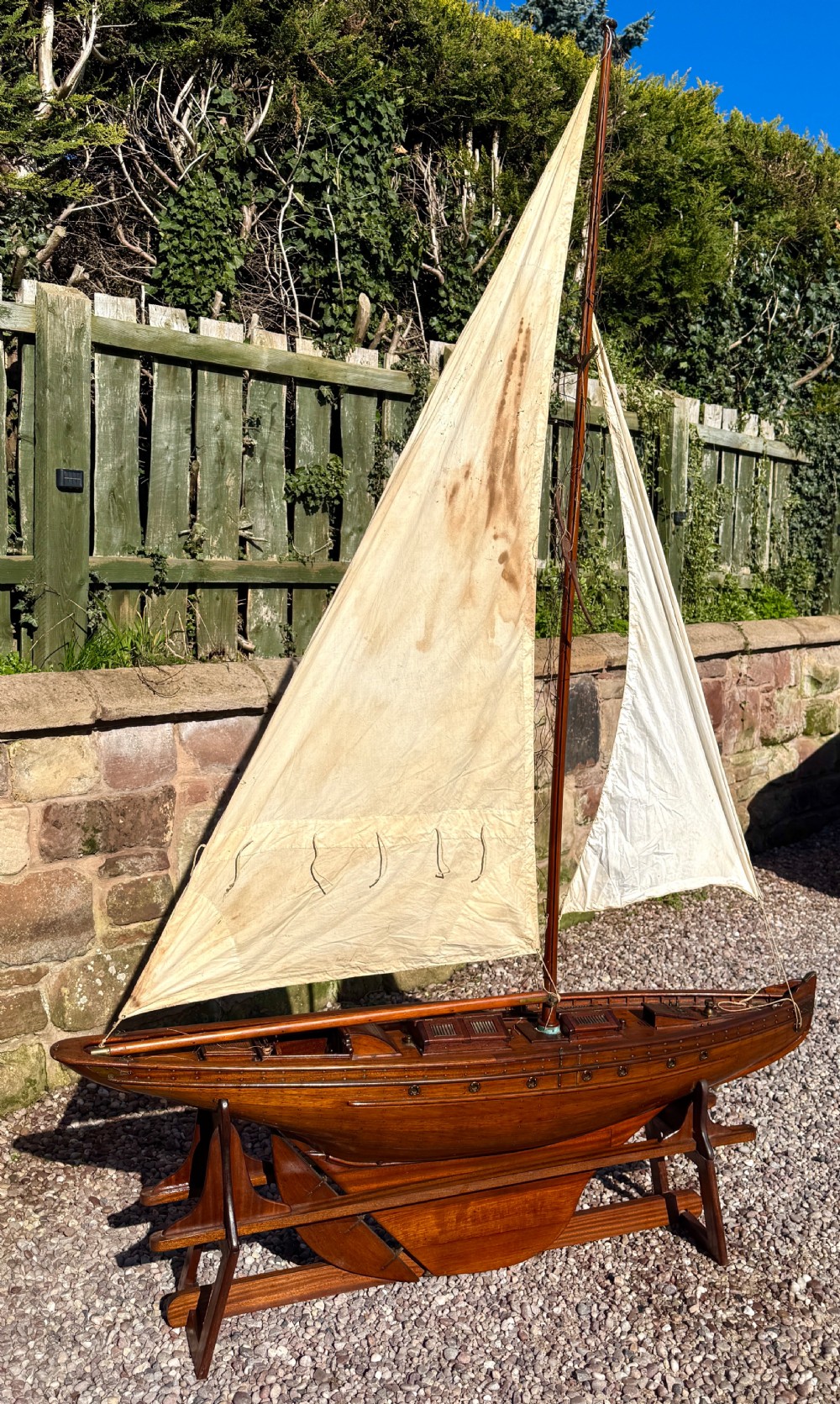 A large Victorian wooden pond yacht with stitched fabric sails, brass deck fittings, and a carved wooden keel, displayed on a wooden stand. View III