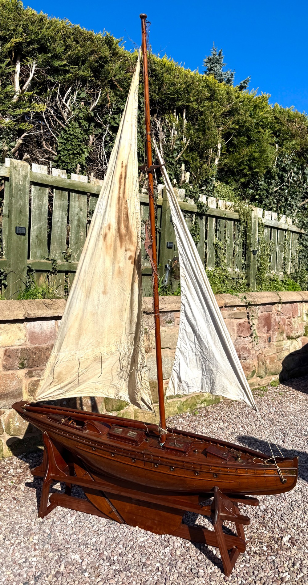 A large Victorian wooden pond yacht with stitched fabric sails, brass deck fittings, and a carved wooden keel, displayed on a wooden stand. View IV