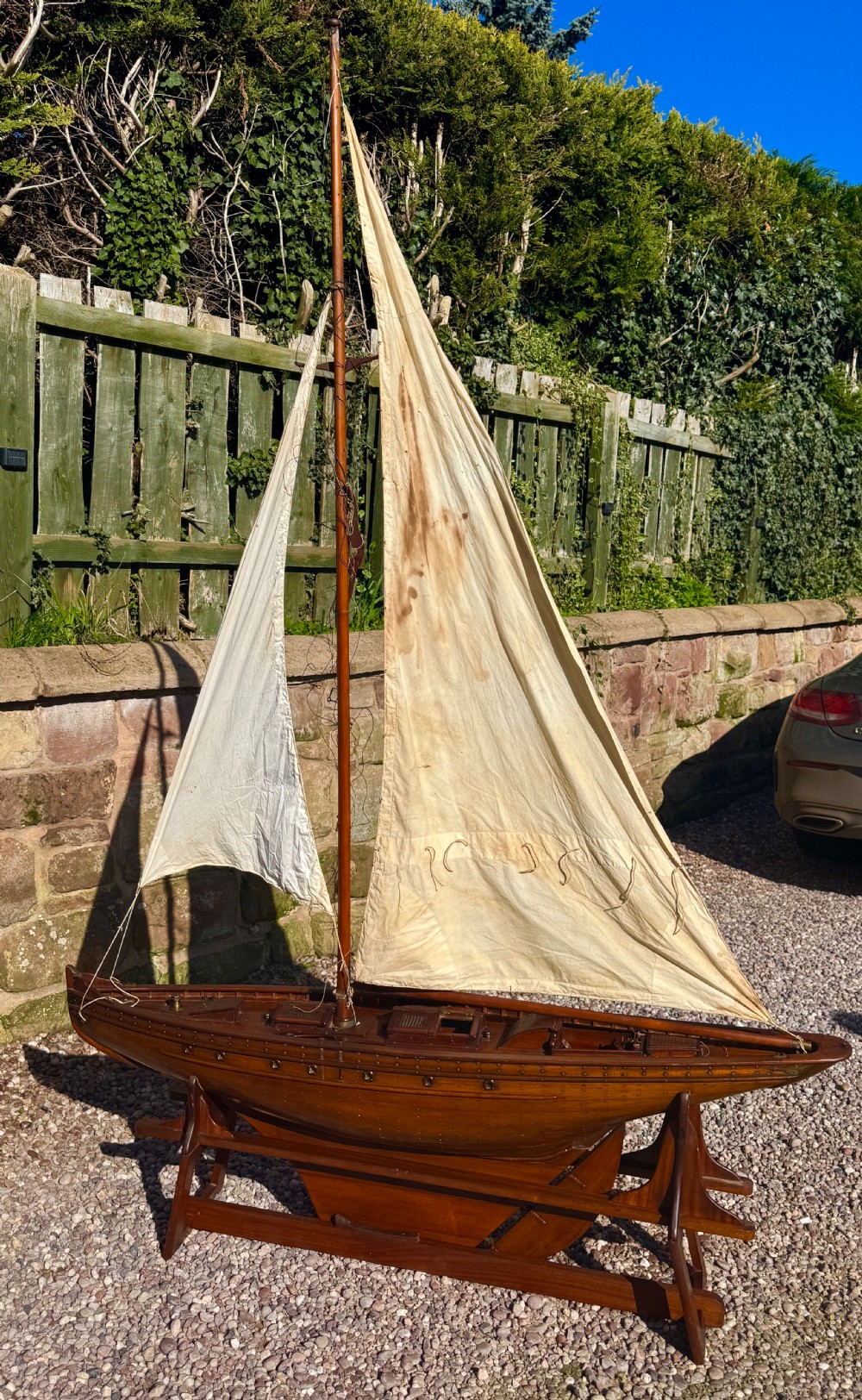A large Victorian wooden pond yacht with stitched fabric sails, brass deck fittings, and a carved wooden keel, displayed on a wooden stand. View VIII