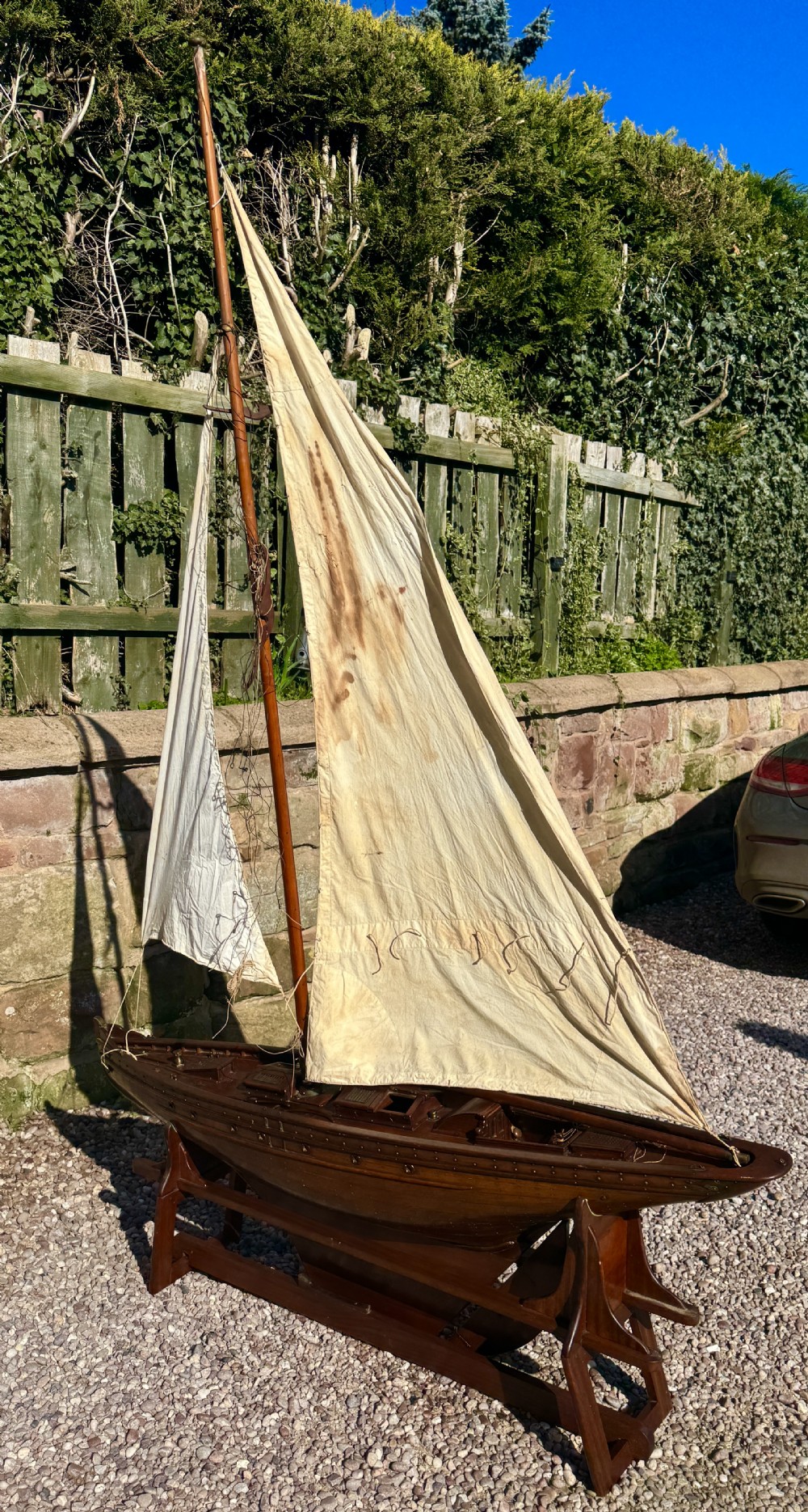 A large Victorian wooden pond yacht with stitched fabric sails, brass deck fittings, and a carved wooden keel, displayed on a wooden stand. View IX