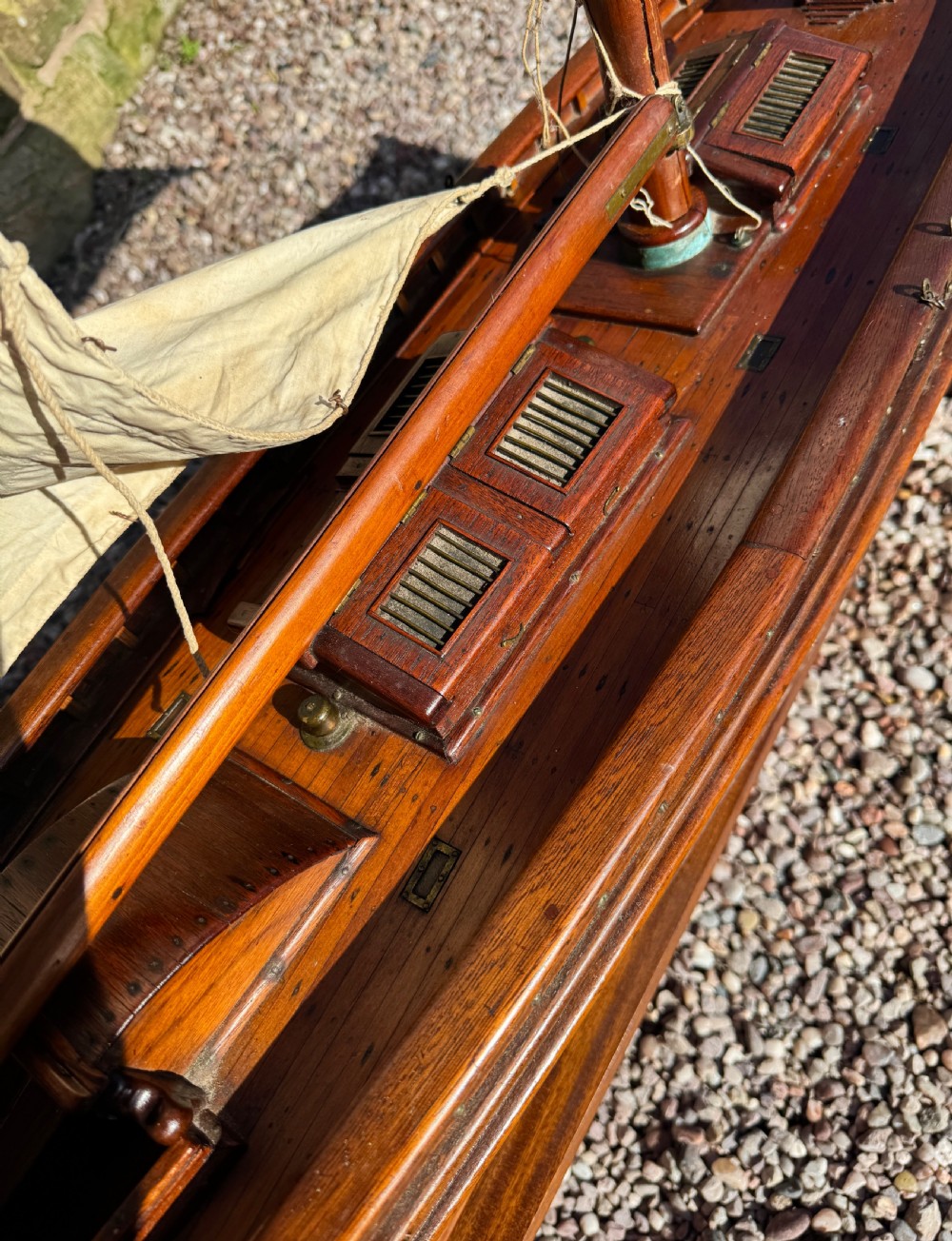 A large Victorian wooden pond yacht with stitched fabric sails, brass deck fittings, and a carved wooden keel, displayed on a wooden stand. View XIV