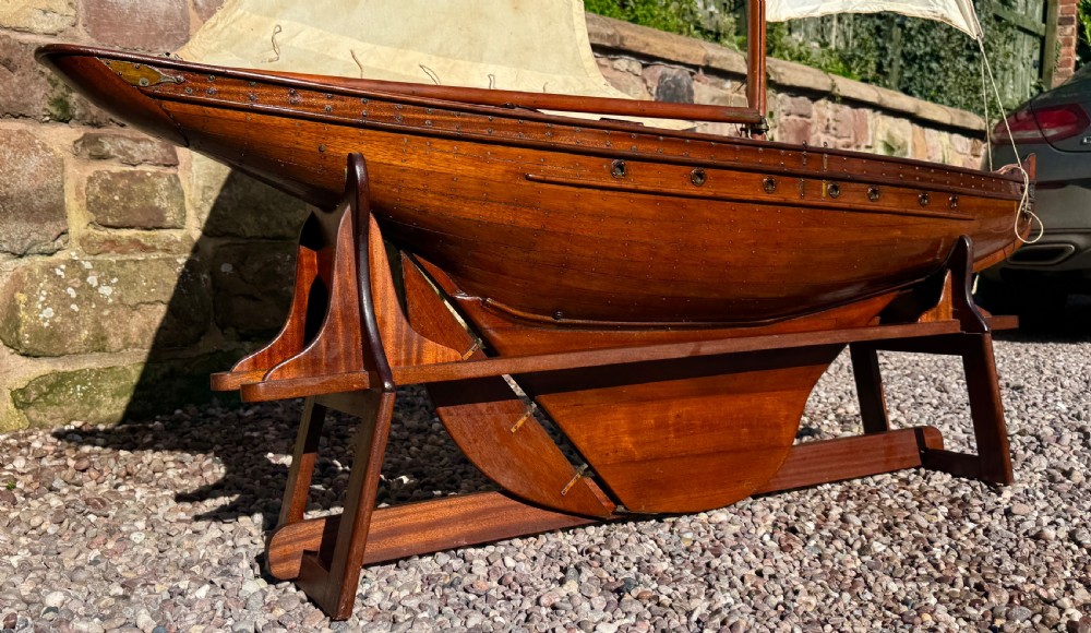 A large Victorian wooden pond yacht with stitched fabric sails, brass deck fittings, and a carved wooden keel, displayed on a wooden stand. View XVI