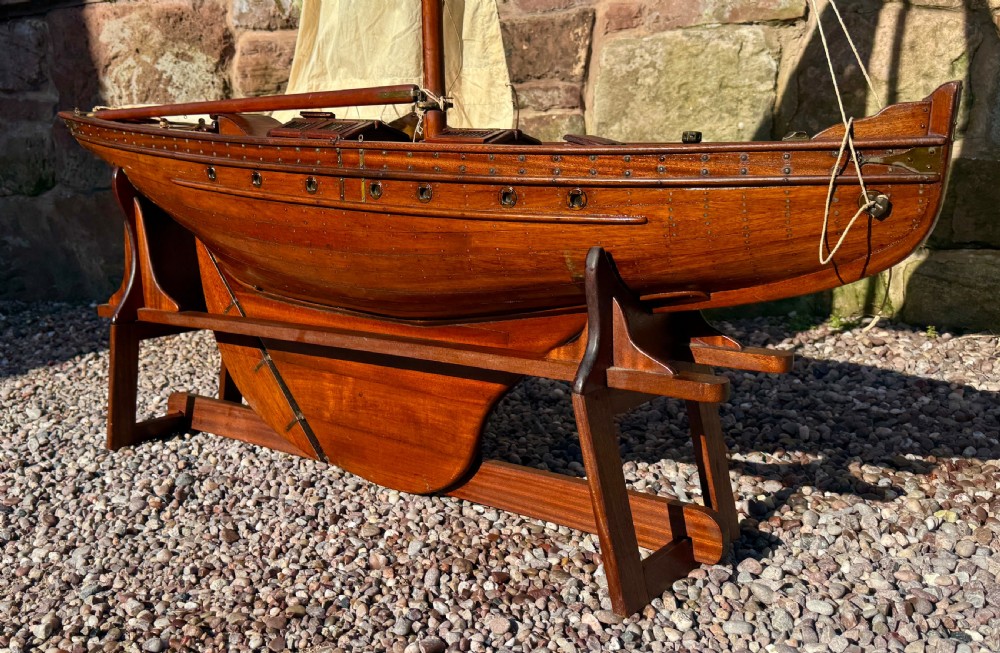 A large Victorian wooden pond yacht with stitched fabric sails, brass deck fittings, and a carved wooden keel, displayed on a wooden stand. View XVII