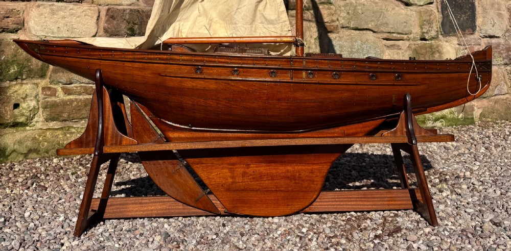 A large Victorian wooden pond yacht with stitched fabric sails, brass deck fittings, and a carved wooden keel, displayed on a wooden stand. View XX