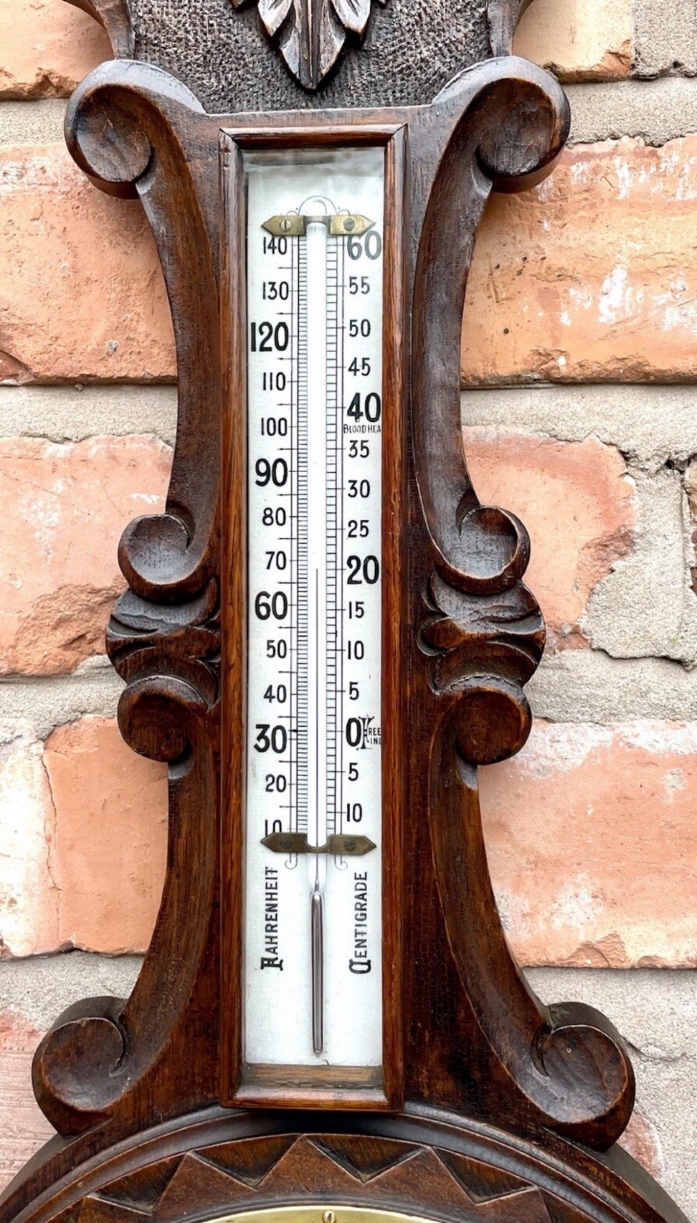 An antique dark carved oak banjo aneroid barometer featuring an upper thermometer tube and a circular brass-rimmed lower dial set into a wooden case. View VIII