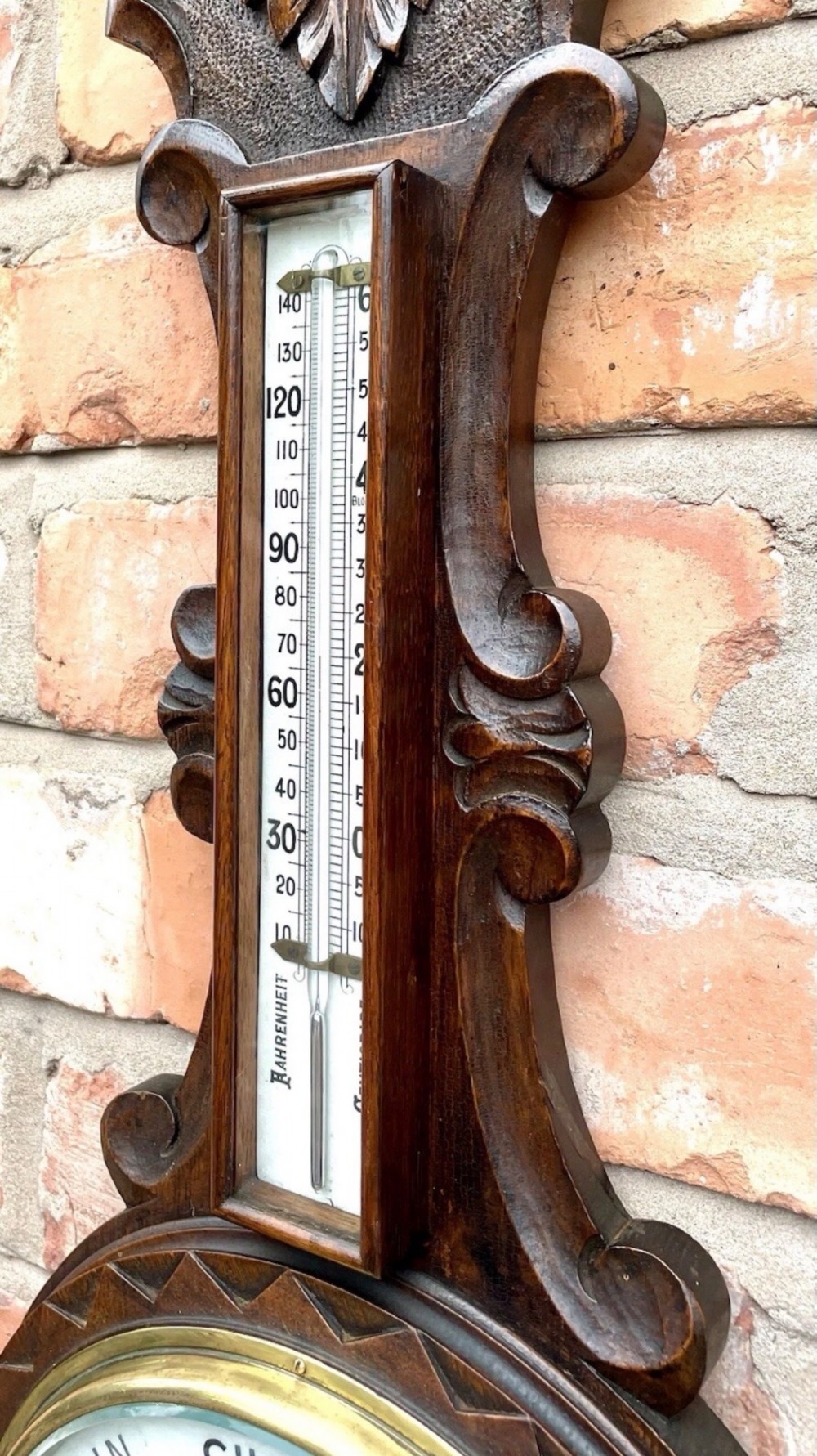 An antique dark carved oak banjo aneroid barometer featuring an upper thermometer tube and a circular brass-rimmed lower dial set into a wooden case. View IX