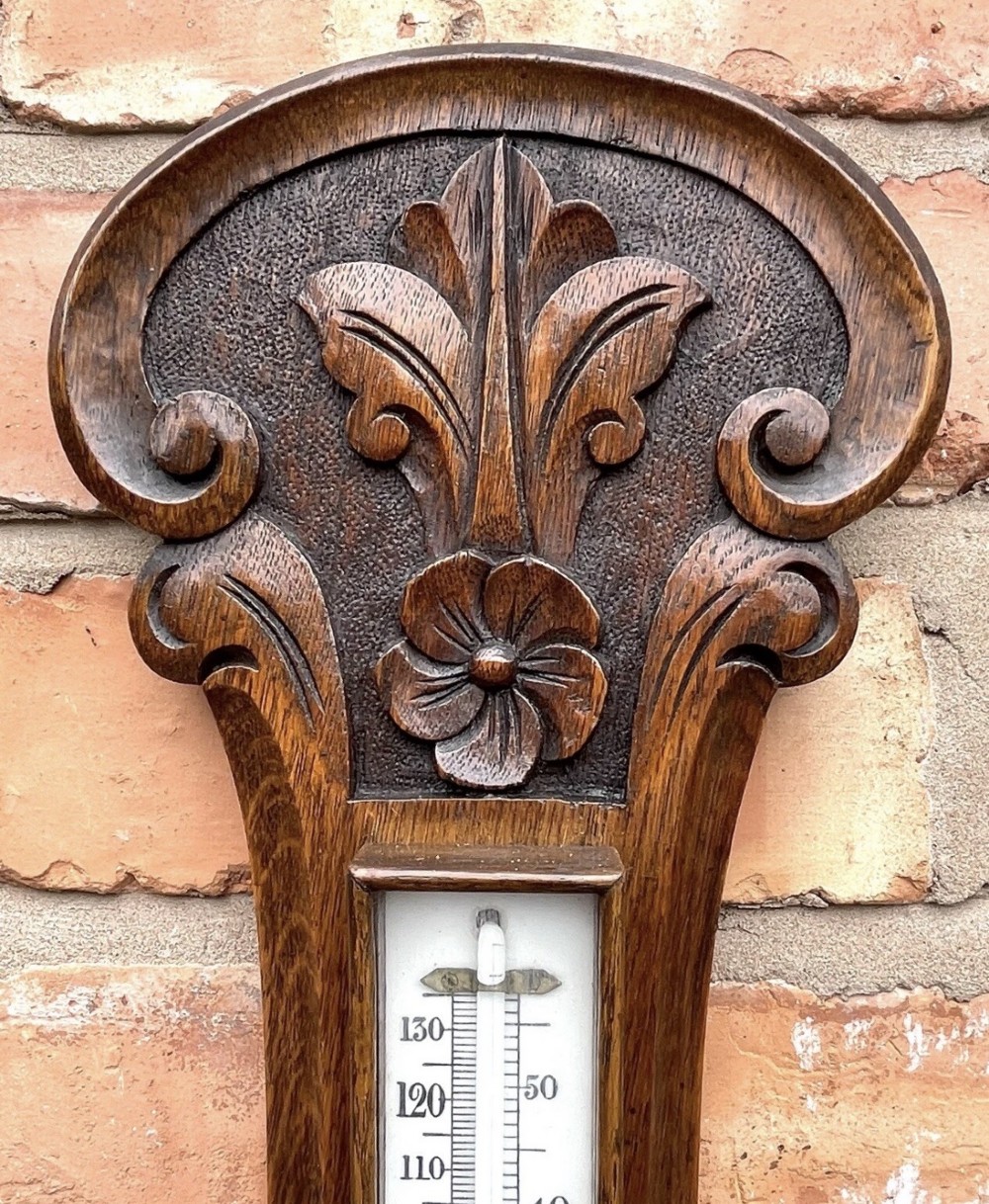 A carved oak banjo-shaped aneroid barometer featuring an integrated glass thermometer tube and decorative foliate carvings. View IV