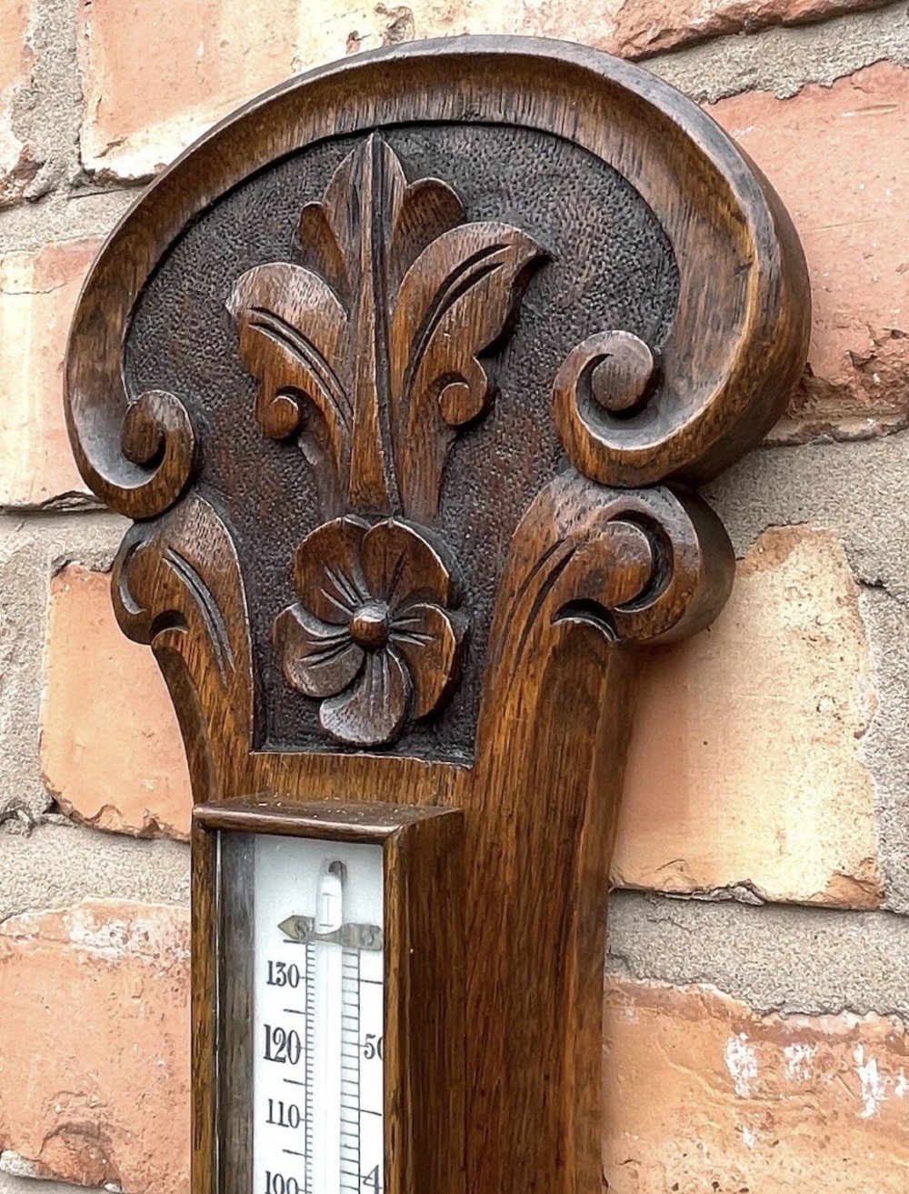 A carved oak banjo-shaped aneroid barometer featuring an integrated glass thermometer tube and decorative foliate carvings. View V
