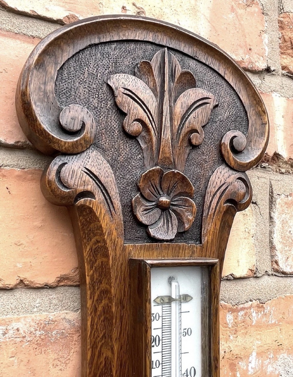 A carved oak banjo-shaped aneroid barometer featuring an integrated glass thermometer tube and decorative foliate carvings. View VI