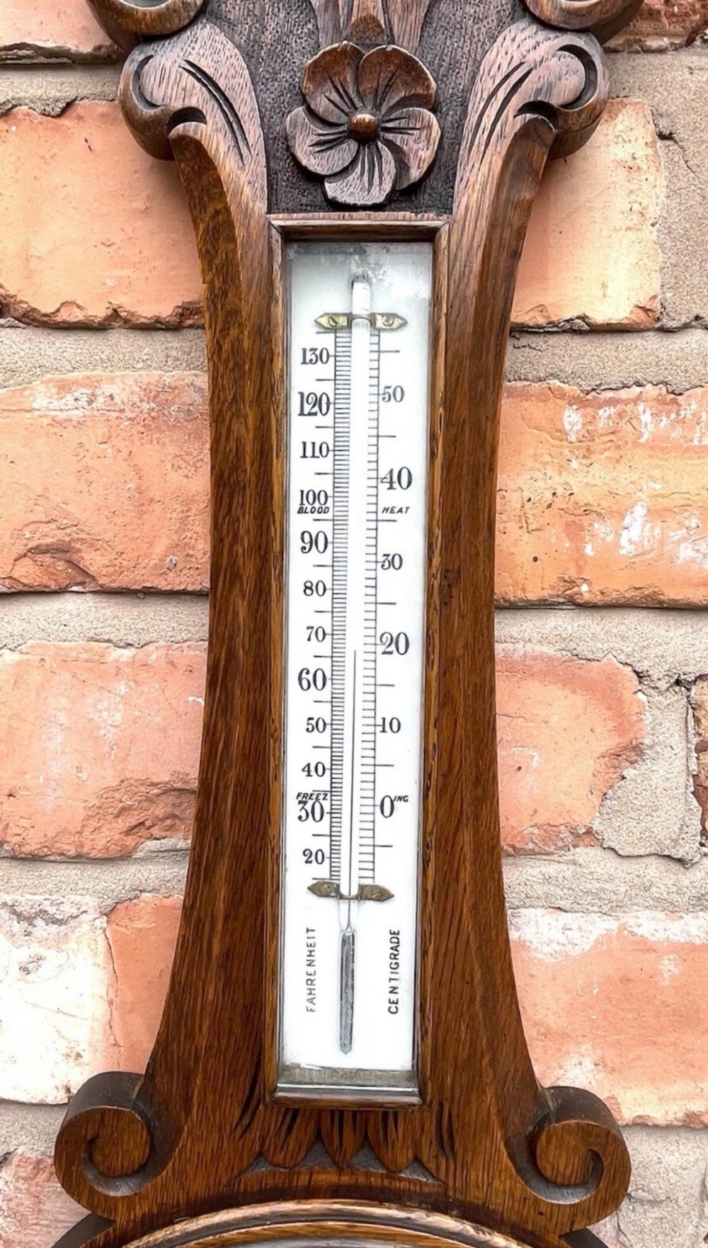 A carved oak banjo-shaped aneroid barometer featuring an integrated glass thermometer tube and decorative foliate carvings. View VII