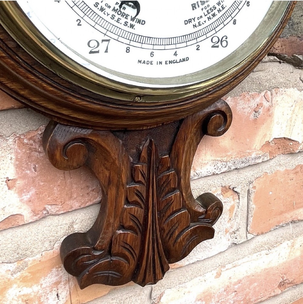 A carved oak banjo-shaped aneroid barometer featuring an integrated glass thermometer tube and decorative foliate carvings. View XIII