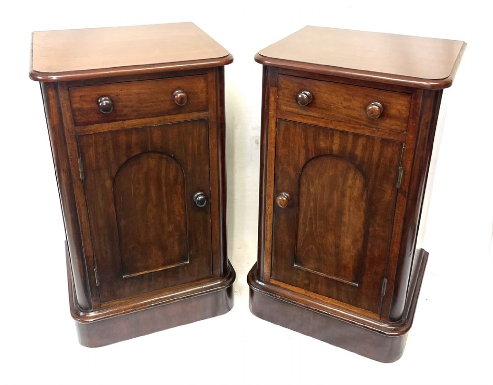 A matching pair of dark mahogany bedside cabinets featuring a top drawer with turned wooden knobs above a recessed arched panel cupboard door set on a plinth base. View II