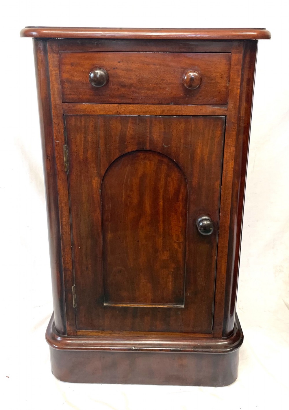 A matching pair of dark mahogany bedside cabinets featuring a top drawer with turned wooden knobs above a recessed arched panel cupboard door set on a plinth base. View V