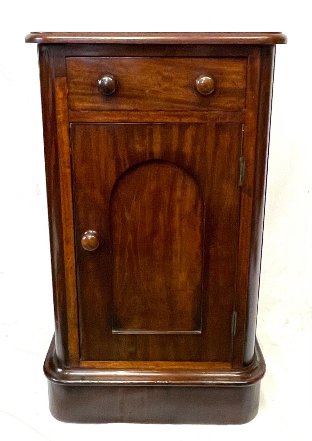 A matching pair of dark mahogany bedside cabinets featuring a top drawer with turned wooden knobs above a recessed arched panel cupboard door set on a plinth base. View VI