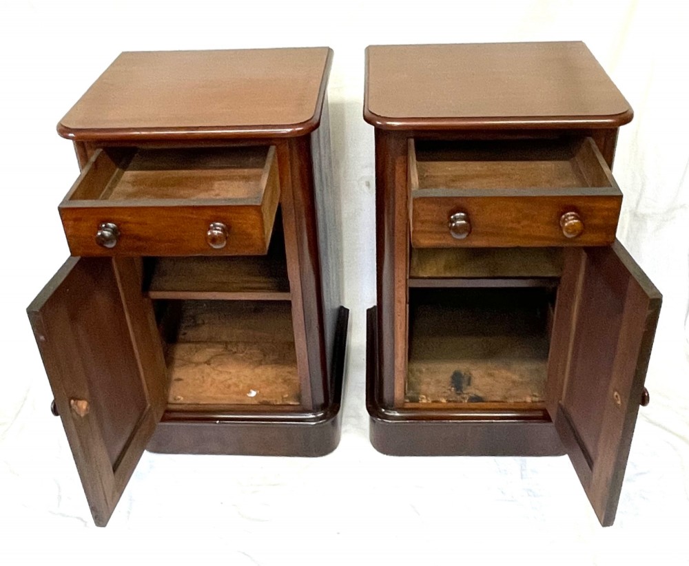 A matching pair of dark mahogany bedside cabinets featuring a top drawer with turned wooden knobs above a recessed arched panel cupboard door set on a plinth base. View VII