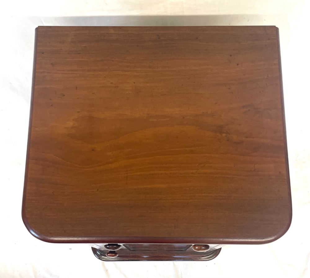 A matching pair of dark mahogany bedside cabinets featuring a top drawer with turned wooden knobs above a recessed arched panel cupboard door set on a plinth base. View X