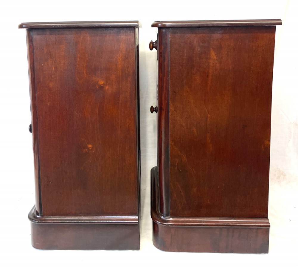 A matching pair of dark mahogany bedside cabinets featuring a top drawer with turned wooden knobs above a recessed arched panel cupboard door set on a plinth base. View XI