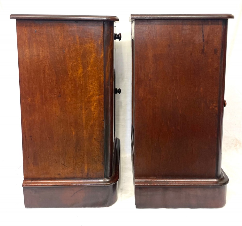 A matching pair of dark mahogany bedside cabinets featuring a top drawer with turned wooden knobs above a recessed arched panel cupboard door set on a plinth base. View XII