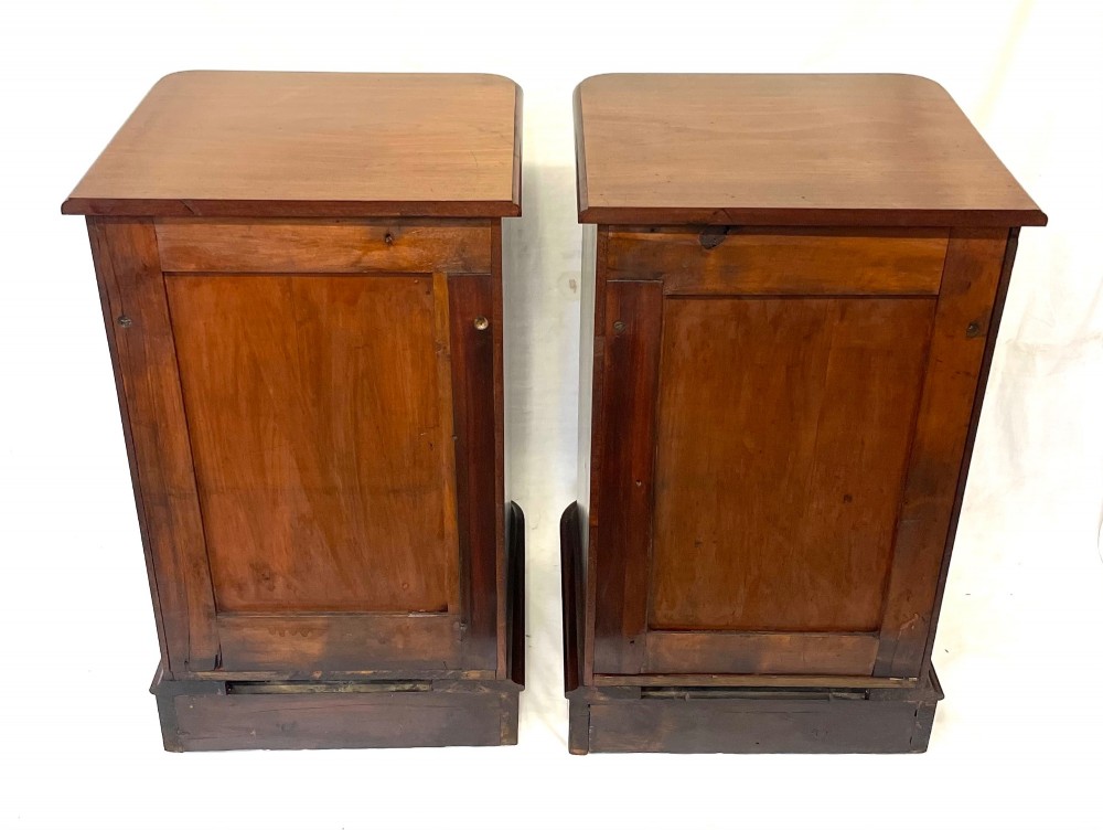 A matching pair of dark mahogany bedside cabinets featuring a top drawer with turned wooden knobs above a recessed arched panel cupboard door set on a plinth base. View XIV