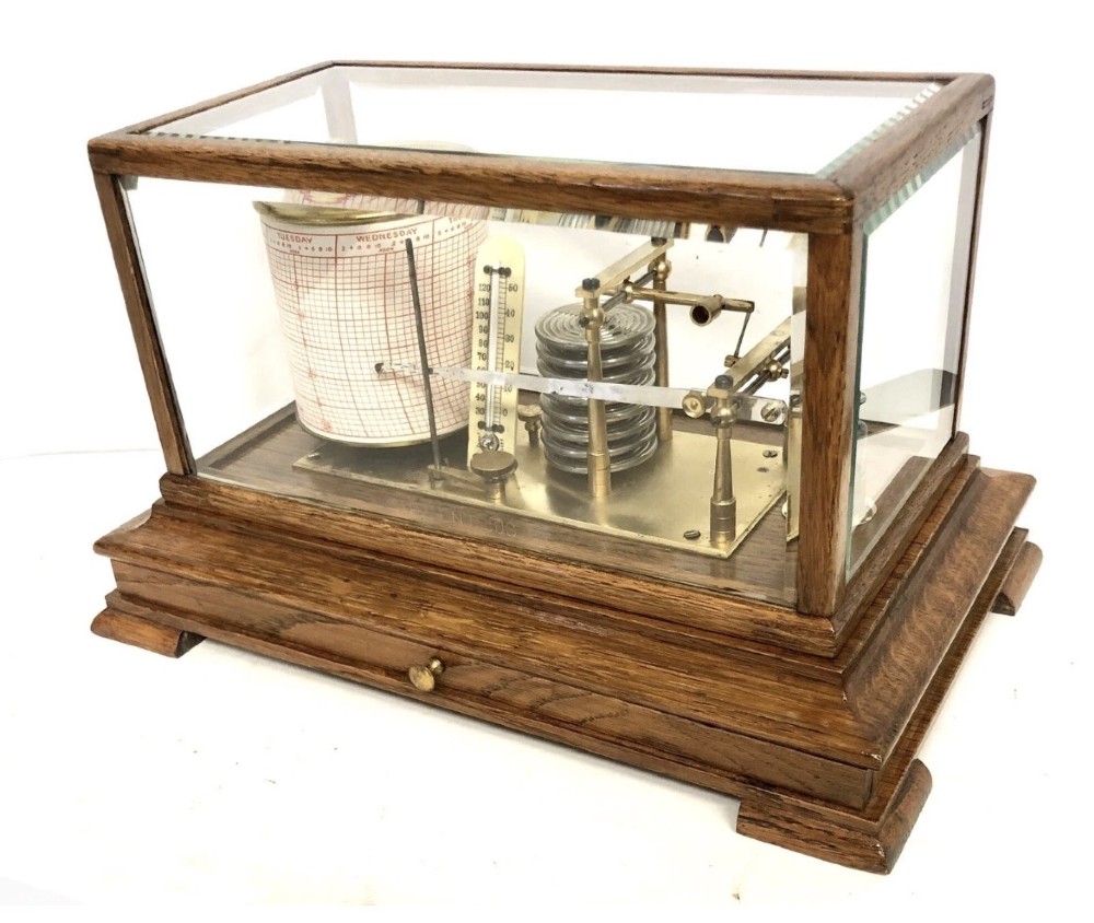 An antique oak cased barograph featuring a brass recording mechanism, internal thermometer, and bevelled glass cover over a base chart drawer.
