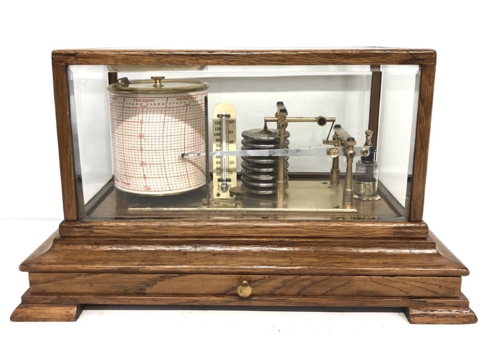 An antique oak cased barograph featuring a brass recording mechanism, internal thermometer, and bevelled glass cover over a base chart drawer. View II